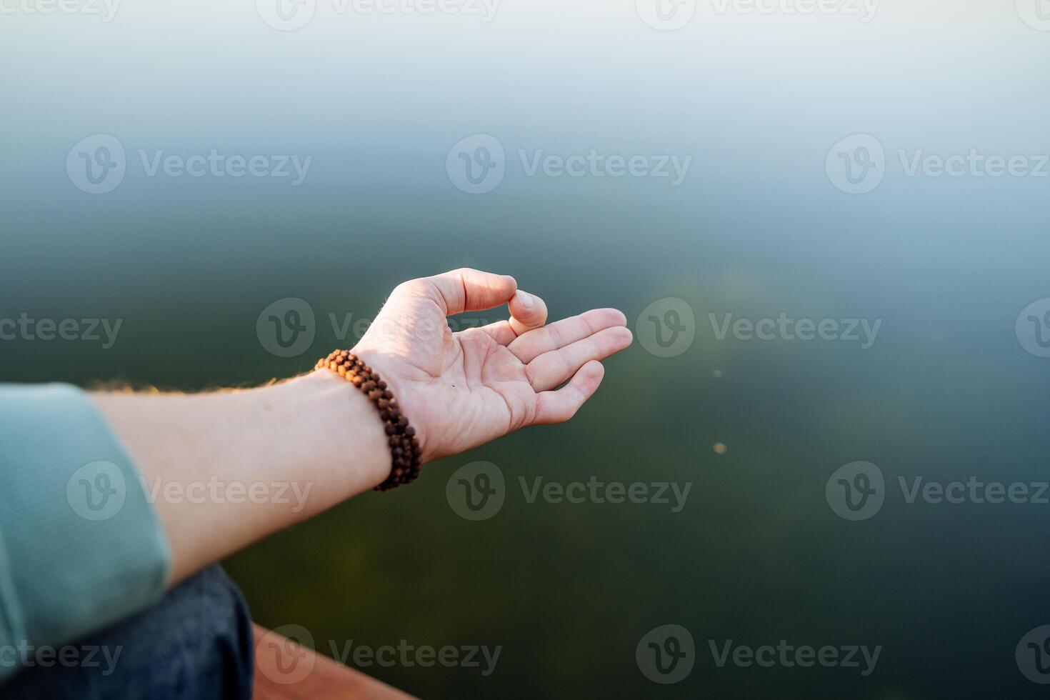 The hand shows the element of yoga, the practice of meditation in silence, the fingers of the hand against the background of the water, yoga on the sea in the summer, put the symbol on the hand photo