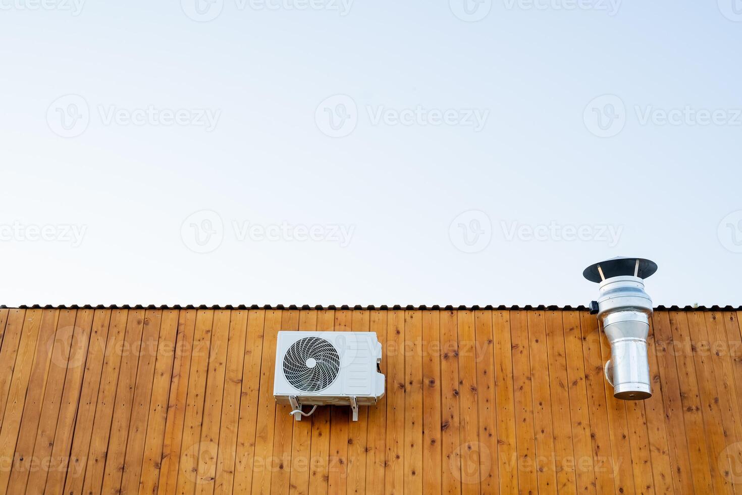 The air conditioner hangs on the back wall of the building, the wooden facade of the cafe hangs a smoke extractor, a chimney ventilation of the room, an air cooling system. photo