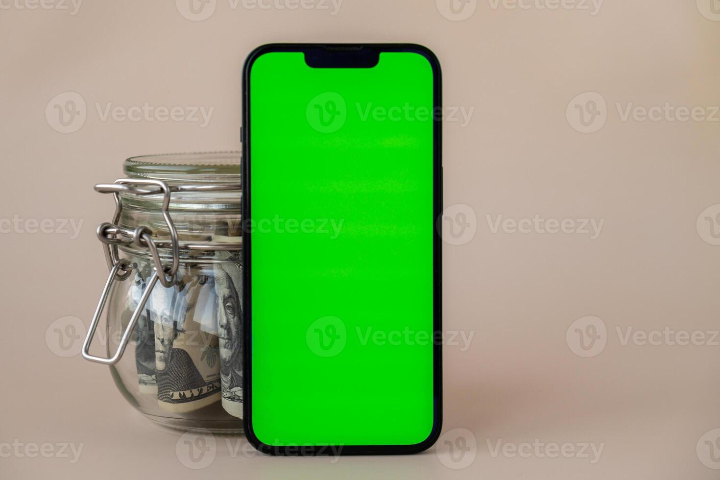 Chrome key smartphone screen mock up template in vertical position on beige background. Copy space App website advertising. Jar filled with dollars cash. Concept of Mobile application and technology business savings. photo