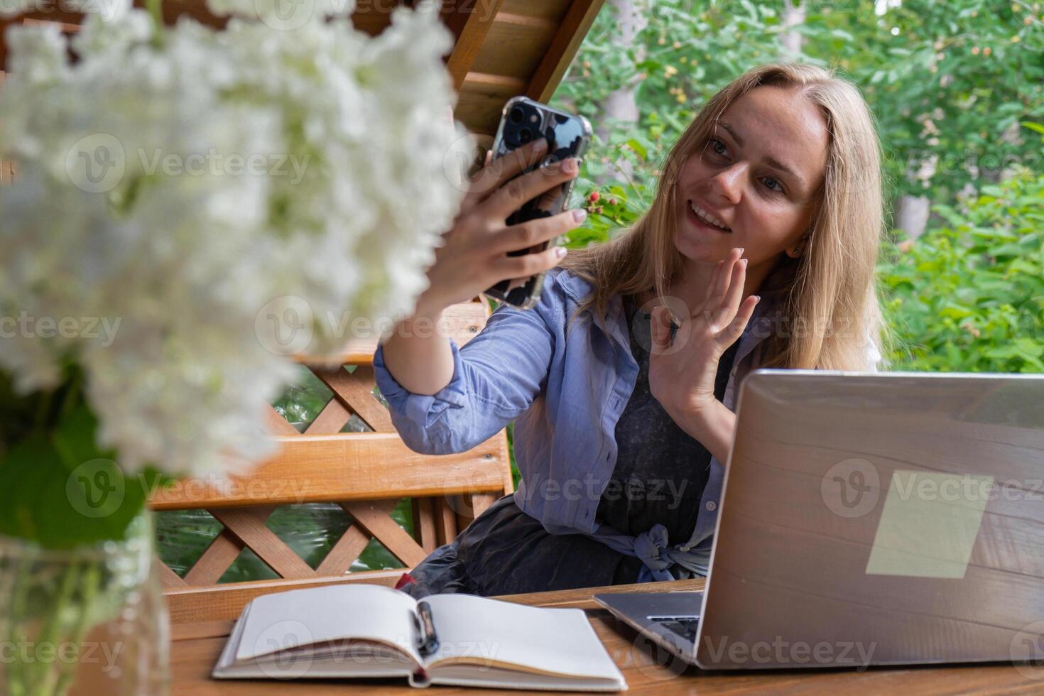 Young happy woman making call on smartphone in wooden alcove. Relaxed outdoor setting emphasizes comfort and productivity. Remote work learning concept photo