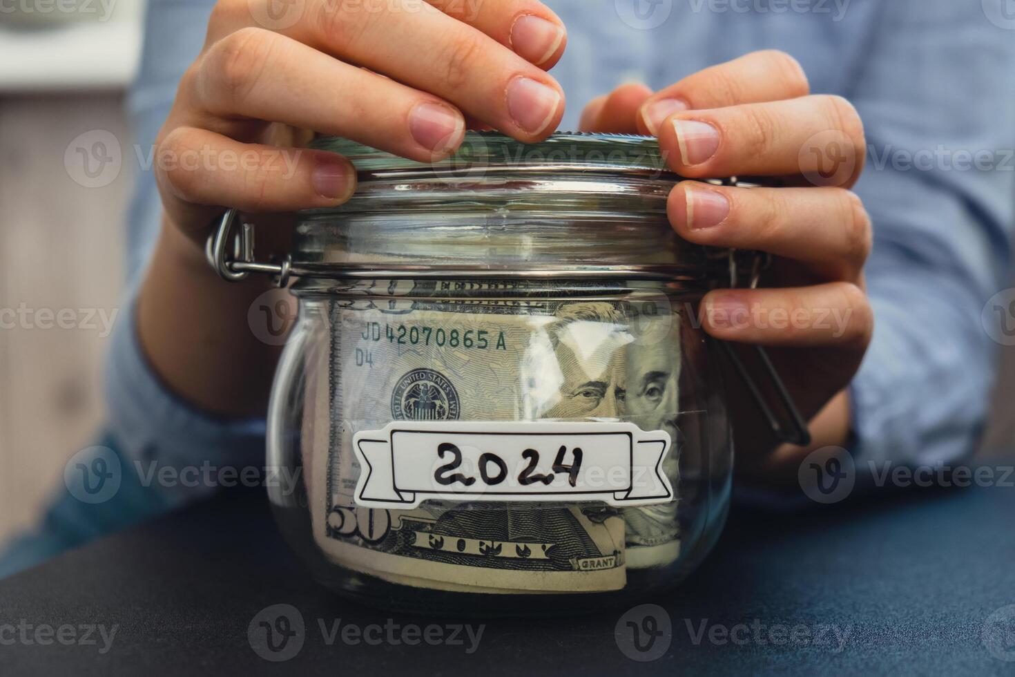 Unrecognizable woman holding Saving Money In Glass Jar filled with Dollars banknotes. 2024 transcription in front of jar. Managing personal finances extra income for future insecurity background photo