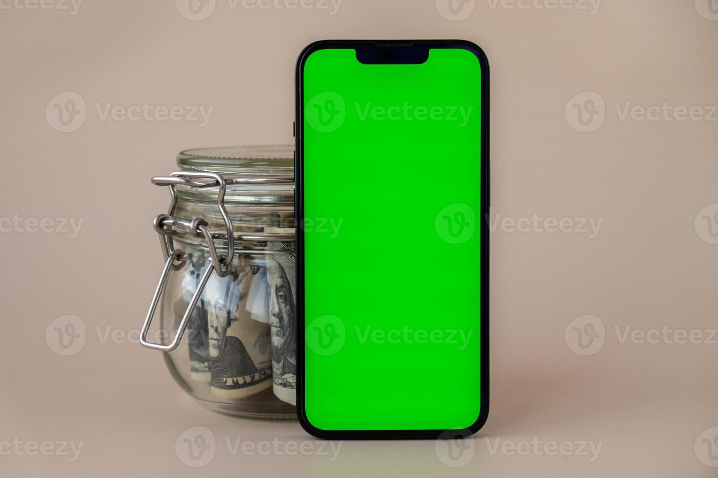 vertical verde pantalla en moderno móvil teléfono en antecedentes de vaso tarro lleno de americano moneda dólar billetes en beige antecedentes. capa pluvial espacio para texto. anuncio para solicitud sitio web. concepto de dinero economía bancos y finanzas foto