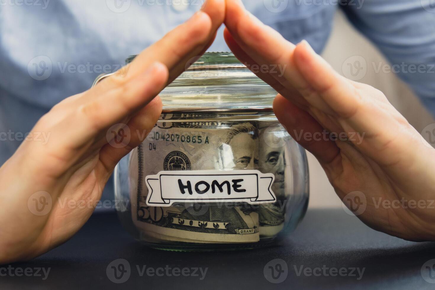 Unrecognizable woman holding Saving Money In Glass Jar filled with Dollars banknotes. HOME transcription in front of jar. Managing personal finances extra income for future insecurity background photo