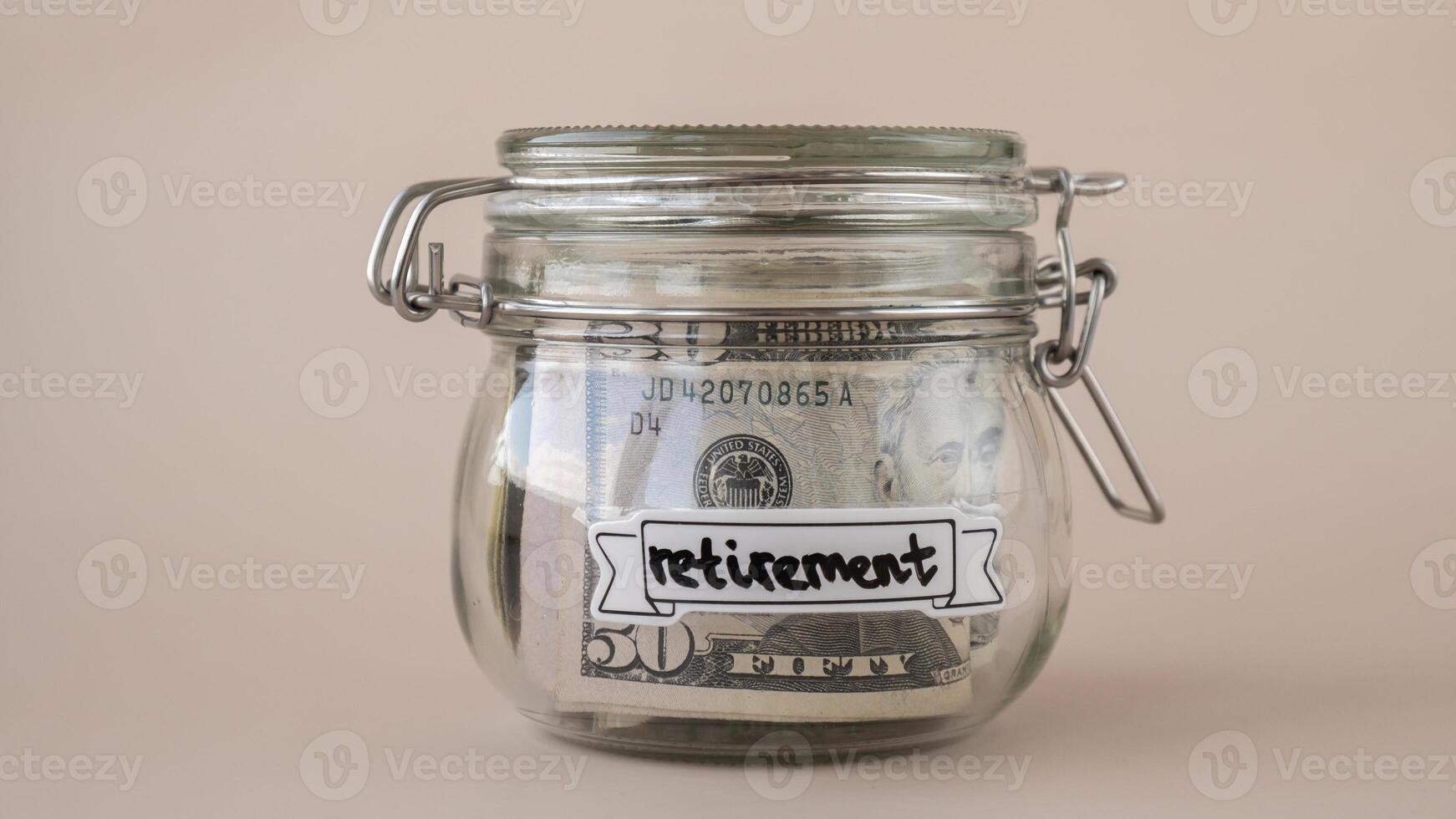 Saving Money In Glass Jar filled with Dollars banknotes. RETIREMENT transcription in front of jar. Managing personal finances extra income for future insecurity. Beige background photo