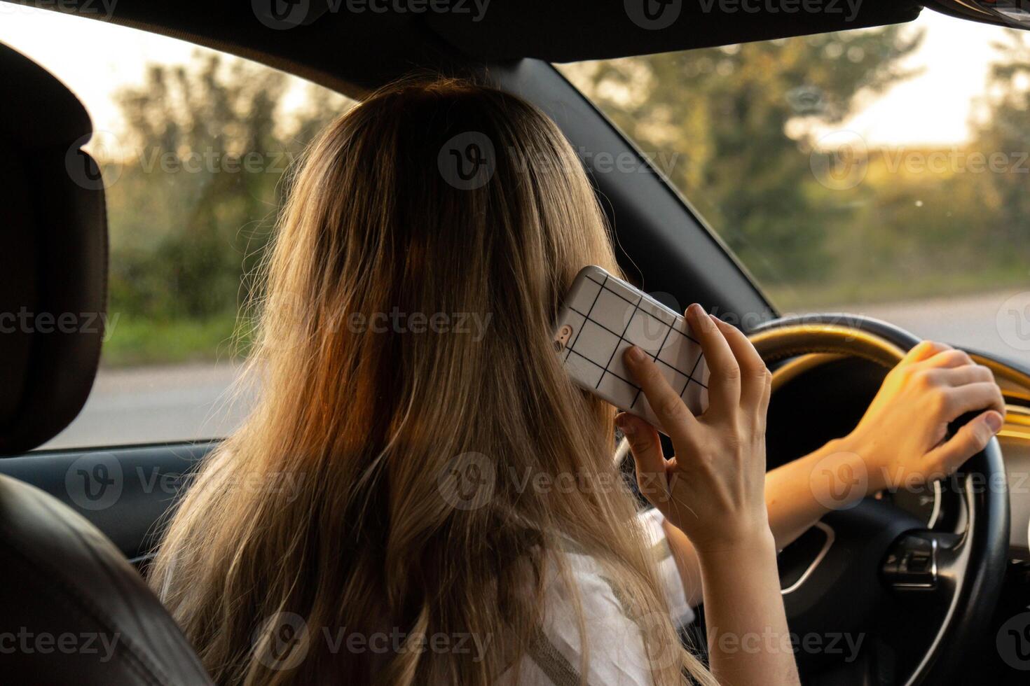 Young woman using mobile phone while driving car on highway road during sunset. Womandriver has accident calling with smartphone for help. Business woman busy driving concept photo
