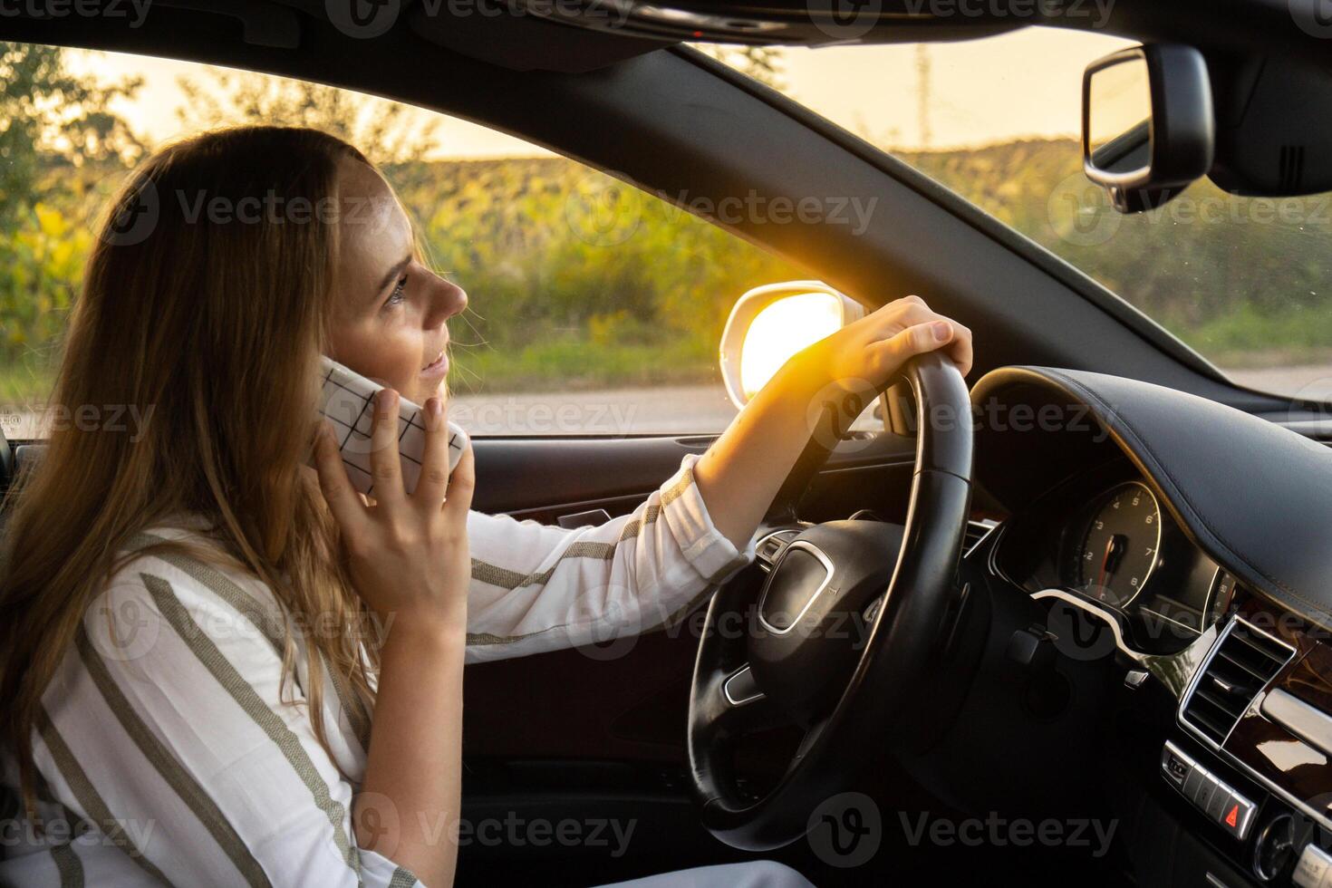 Happy young woman speaking by mobile phone while driving car. Business woman talking phone call in automobile. Unsafely risky driving. Concept of multitasking photo