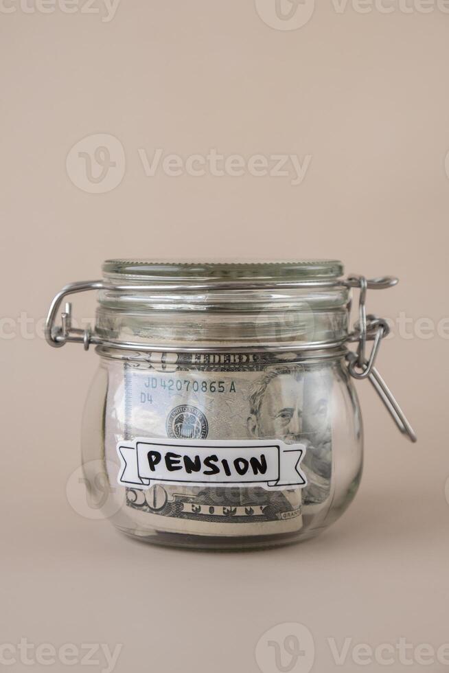 Saving Money In Glass Jar filled with Dollars banknotes. PENSION transcription in front of jar. Managing personal finances extra income for future insecurity. Beige background photo