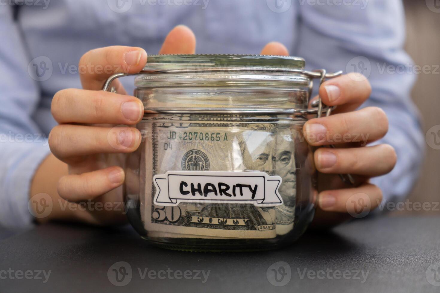 Female hands Saving Money In Glass Jar filled with Dollars banknotes. CHARITY transcription in front of jar. Managing personal finances extra income for future insecurity background photo