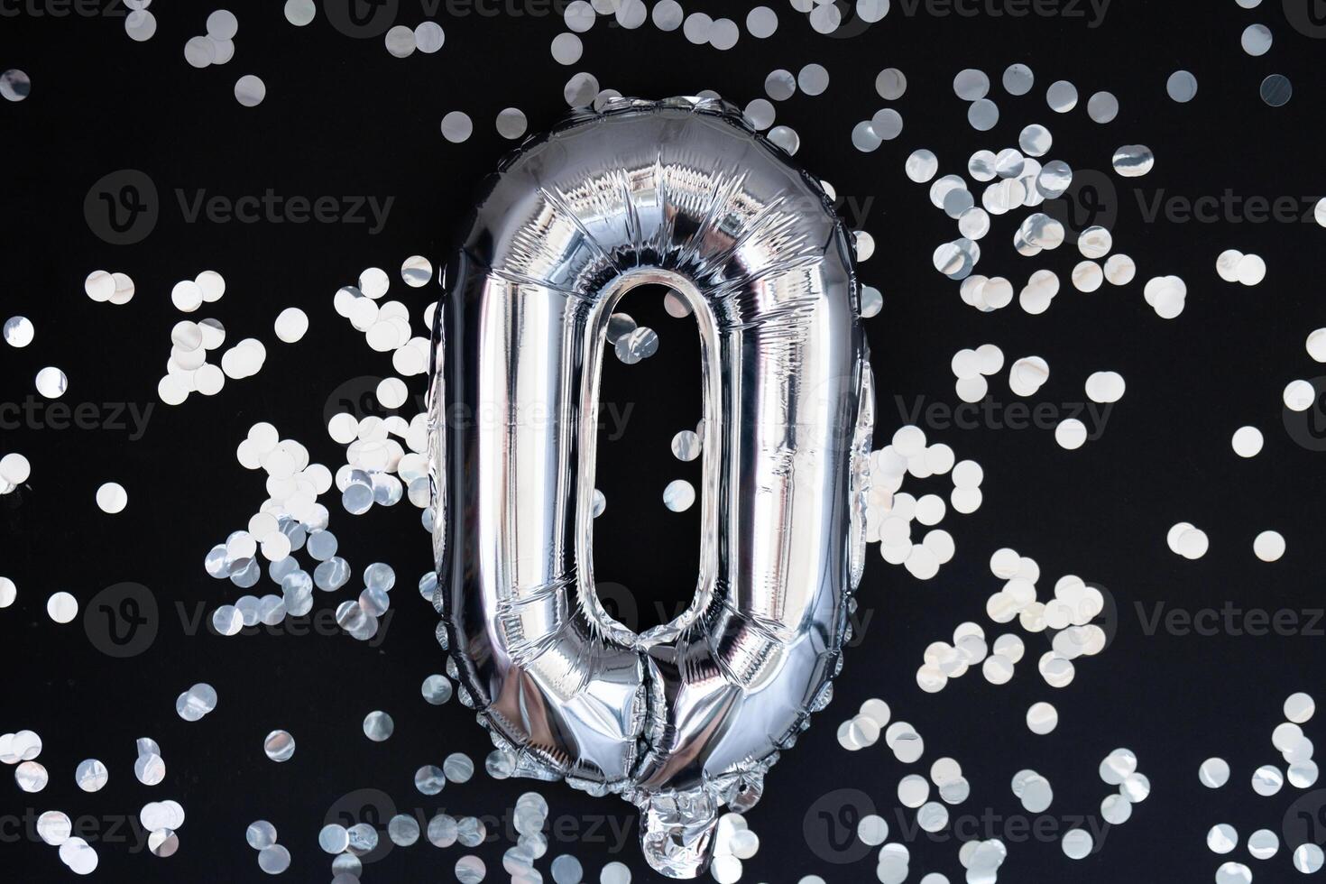 0 zero metallic balloon with sparkling confetti on dark black background. Greeting card silver foil balloon number Happy birthday holiday concept. Copy space for text. Celebration party congratulation decoration photo