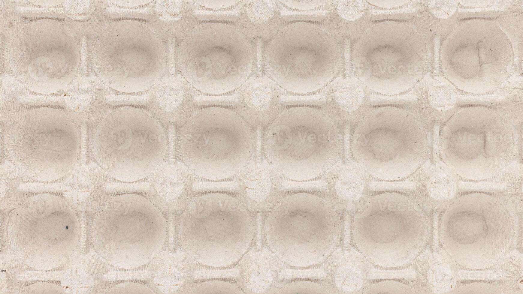 A top view of a beige egg carton displaying symmetrical circular indentations photo