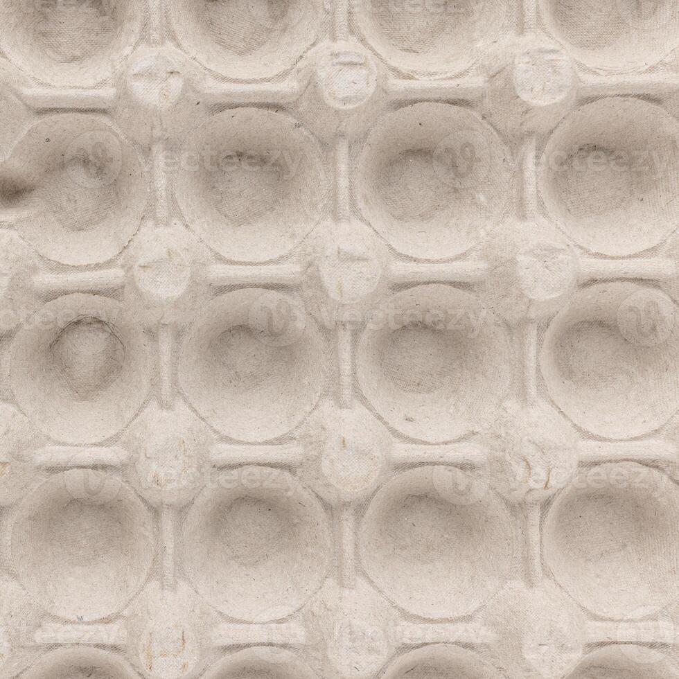 A top view of a beige egg carton displaying symmetrical circular indentations photo