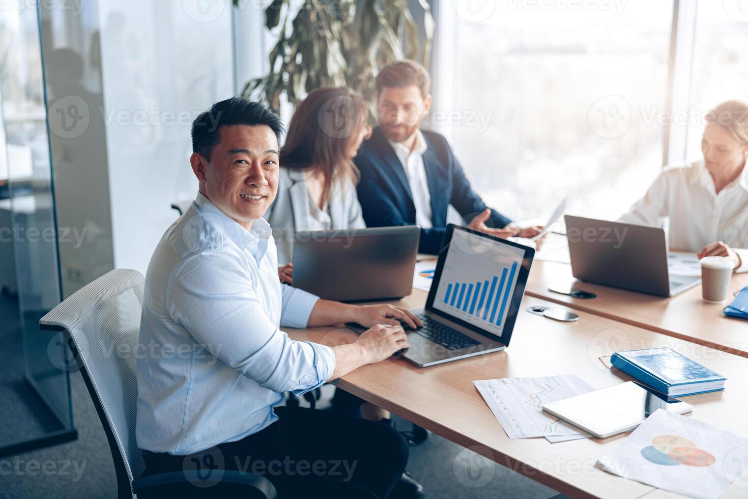 Portrait of smiling asian businessman working on a laptop during a meeting with a team photo
