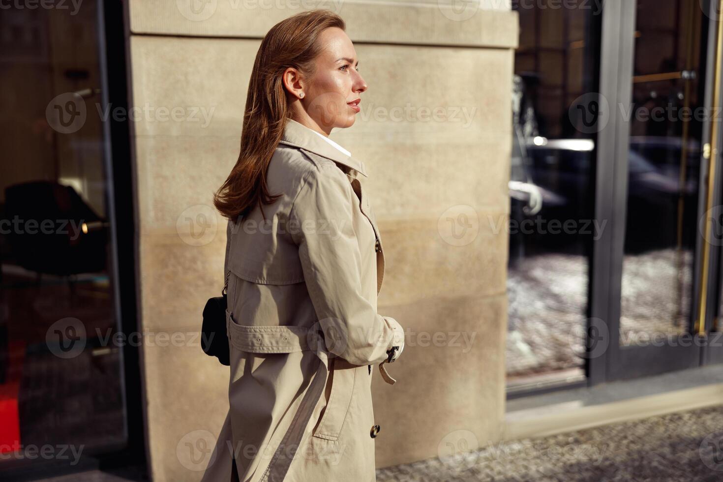 Attractive woman in coat crossing the city street and looking at side. Blurred background photo