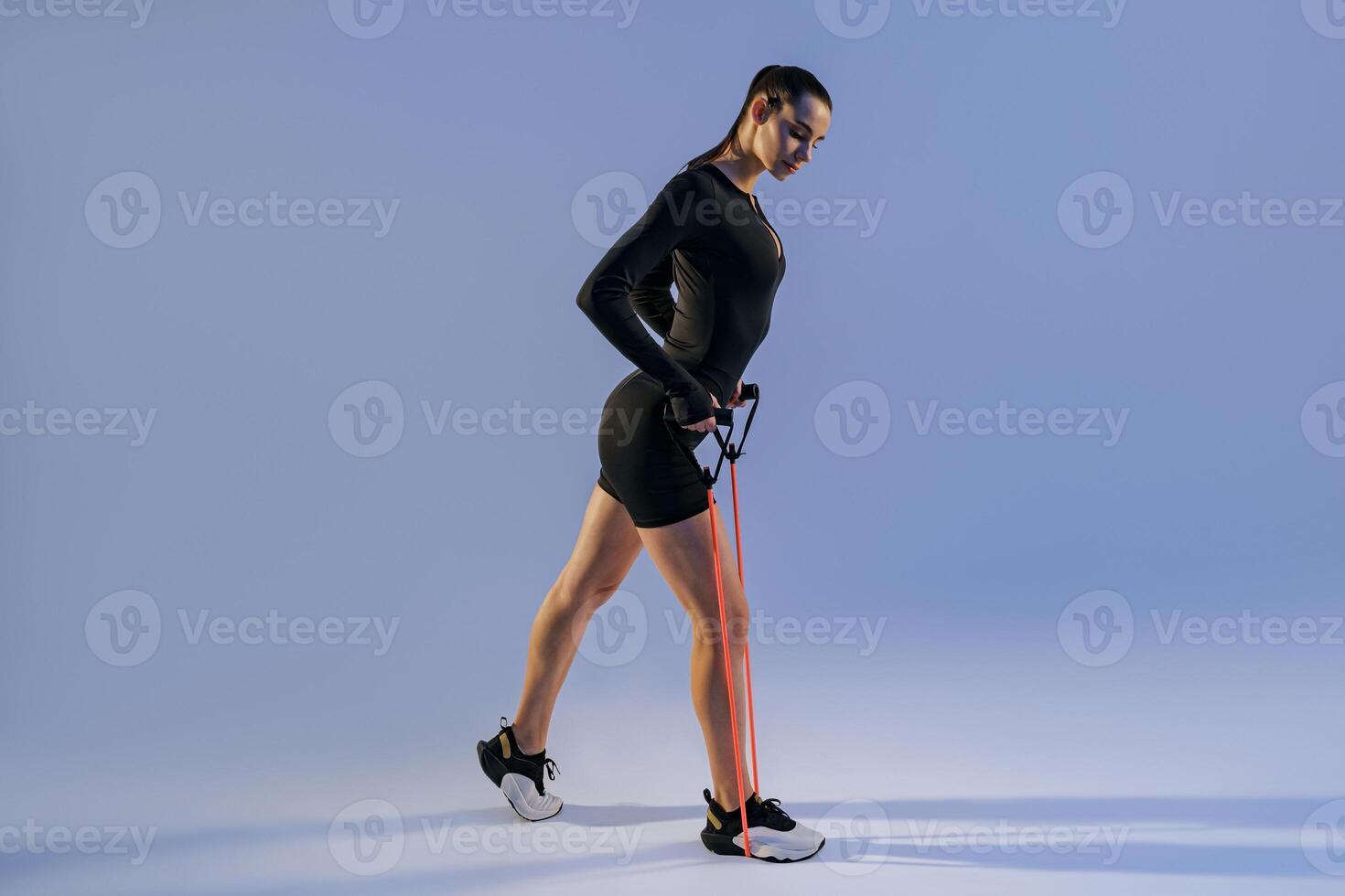 Strong woman in sportswear performs fitness exercises with resistance band on studio background photo