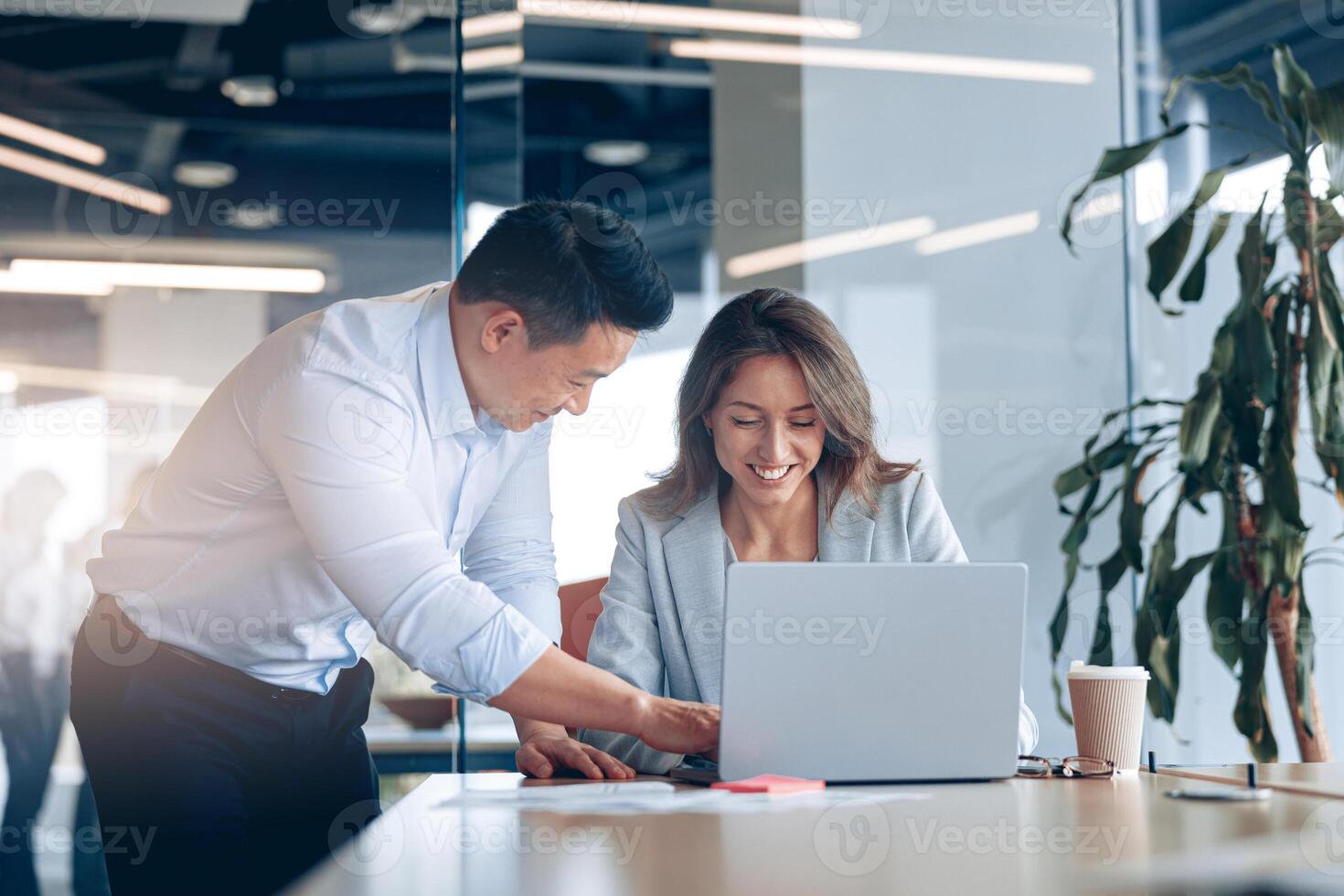 Confident asian office worker discussing work with mature caucasian female businesswoman photo