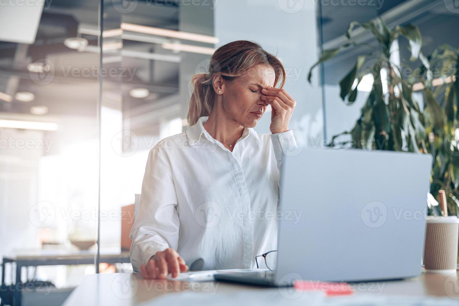 Tired business lady with headache working on laptop at her workplace at modern office photo