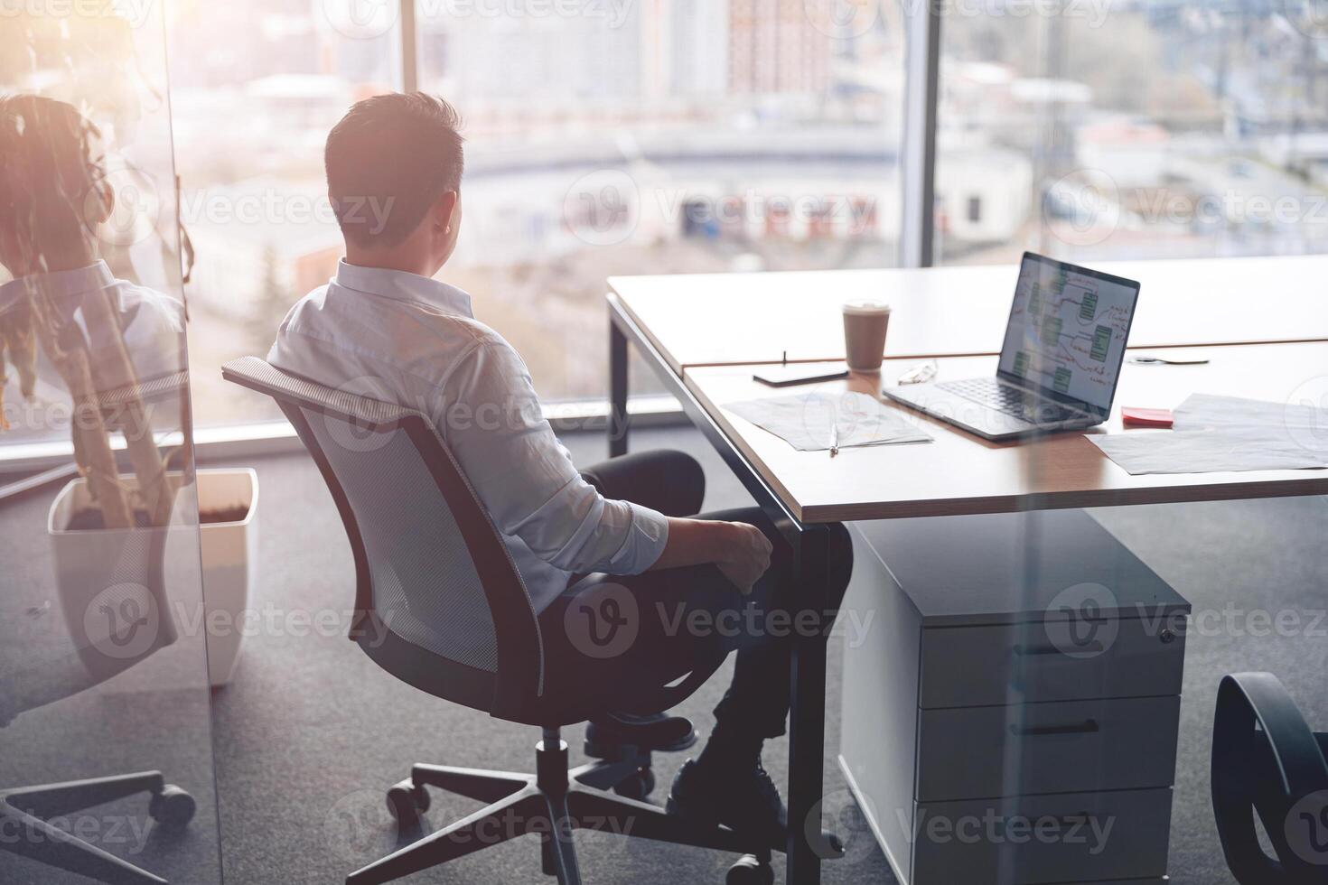 Focused businessman working on laptop and looking out the window at her workplace at modern office photo