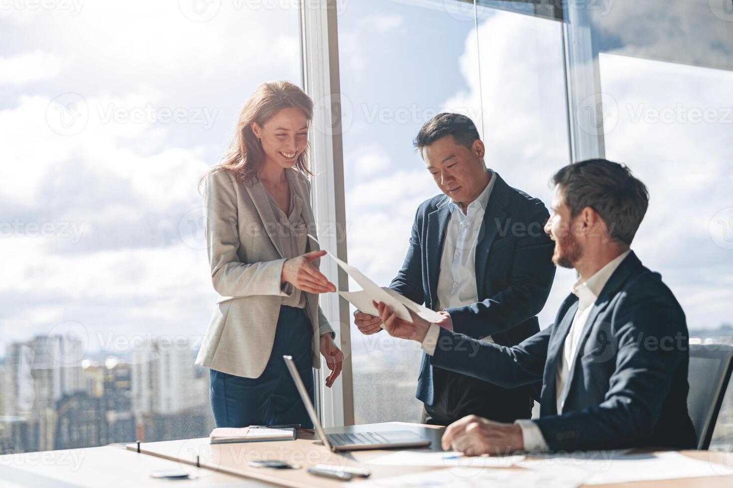 Positive office employees discussing work issues using laptop and documents with graphs and charts photo