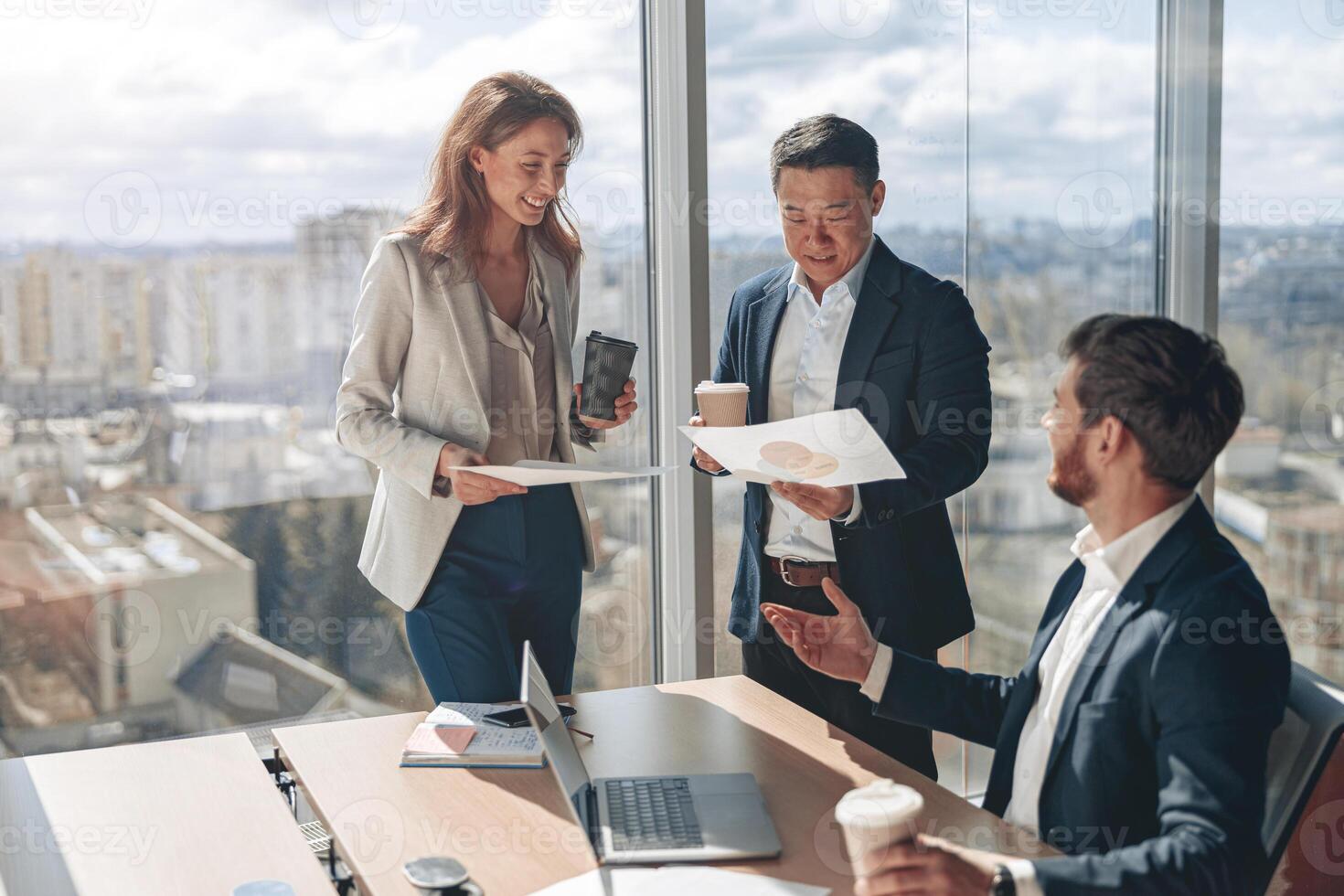 Positive office employees discussing work issues using laptop and documents with graphs photo