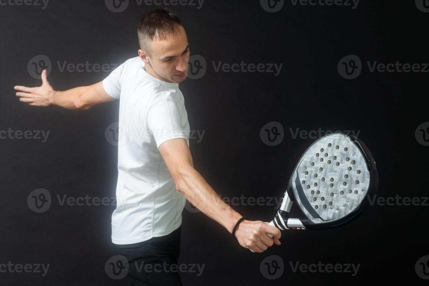 Portrait of man playing paddle tennis in position to hit a backhand ball black isolated background. Front view. photo