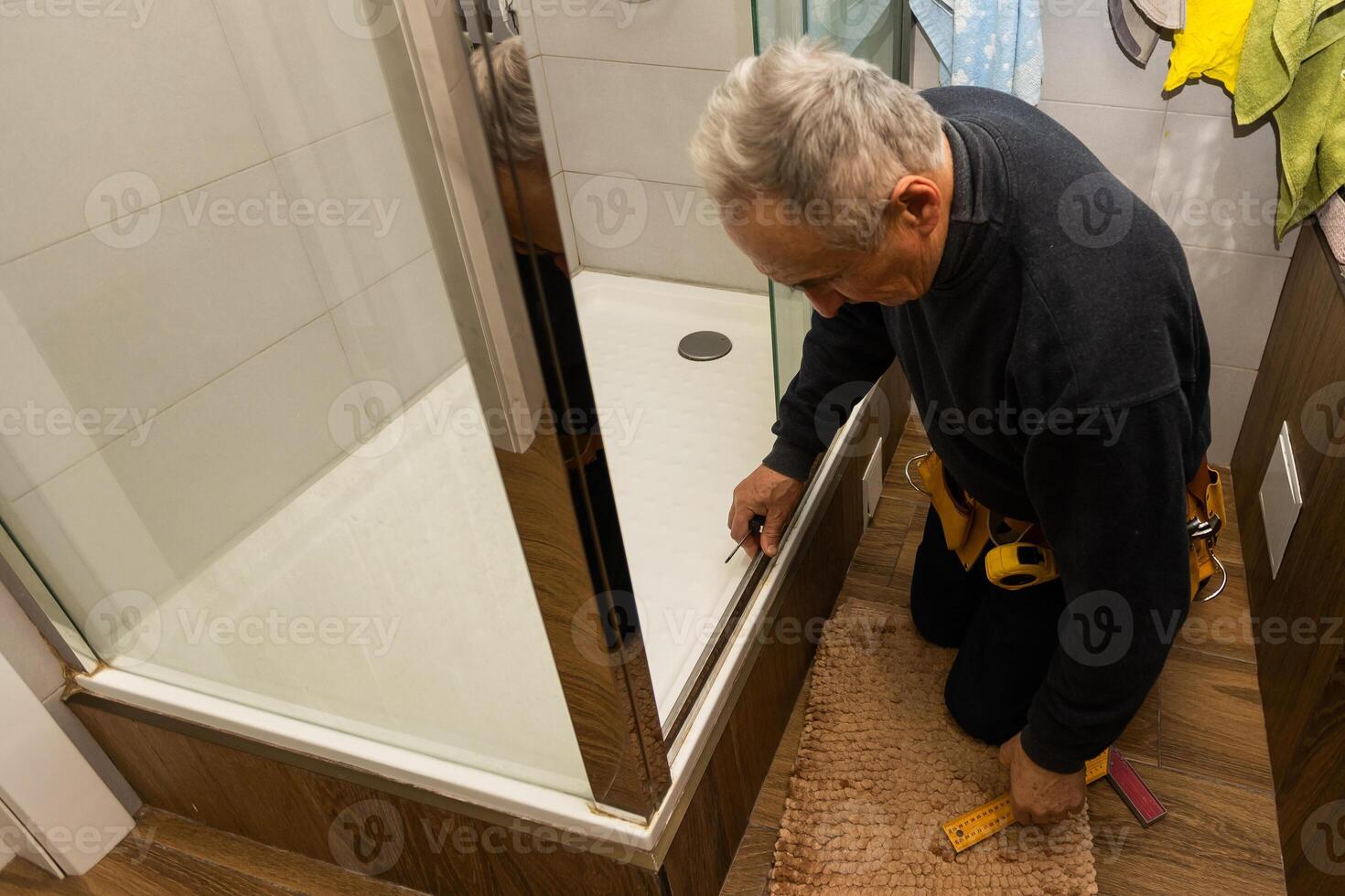 an elderly man repairing door of shower cabin in bathroom photo