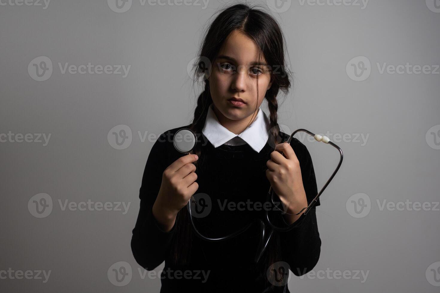 A girl with braids in a gothic style on a dark background with stethoscope. photo