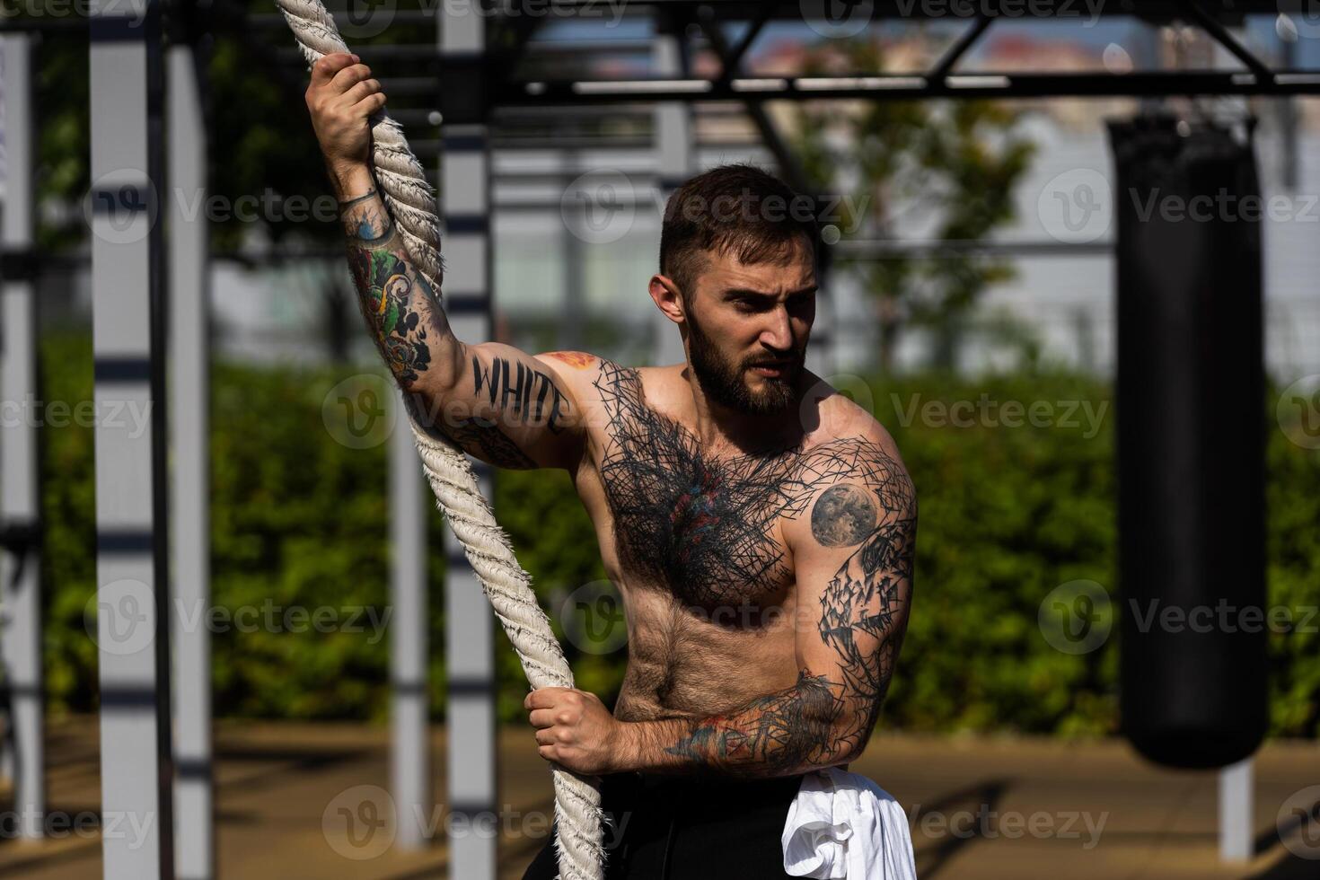 muscular carrocero hermoso hombre con desnudo torso trenes triceps en un Transversal cable ejercicio máquina en el calle foto