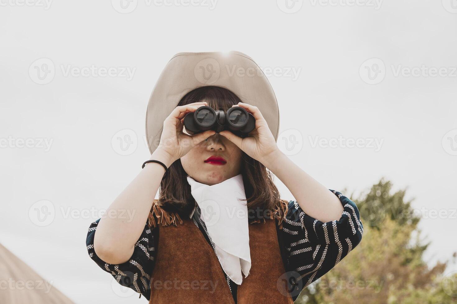 cute chinese cowgirl while looking at the horizon with binoculars photo