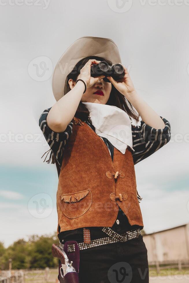 cute chinese cowgirl while looking at the horizon with binoculars photo