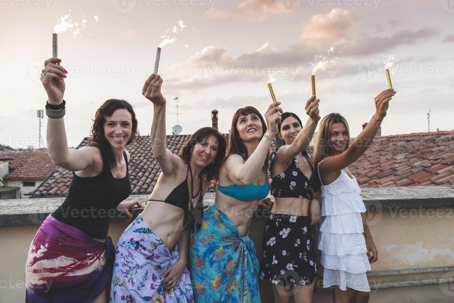 Group of happy female friends holding sparklers at rooftop party photo
