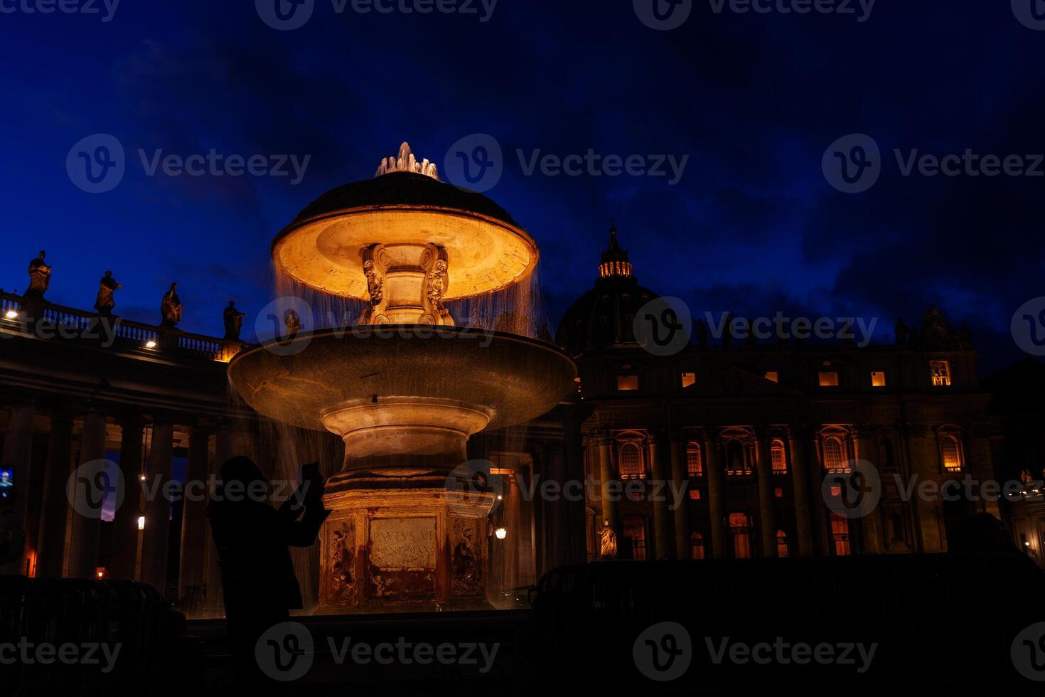 night image of a tourist photographing one of the illuminated fountains in St. Peter's Square photo