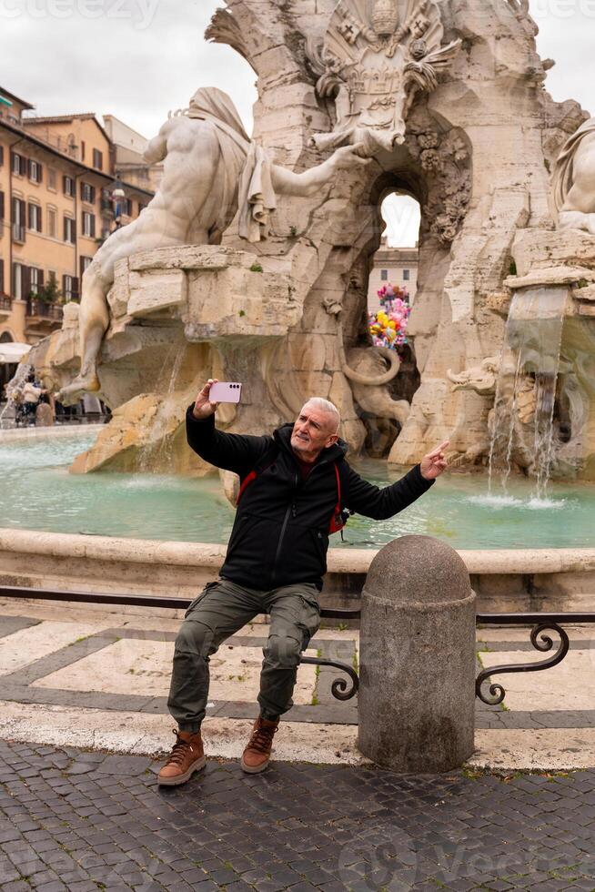 happy middle aged man on vacation taking a selfie in front of the fountain in piazza navona in rome photo