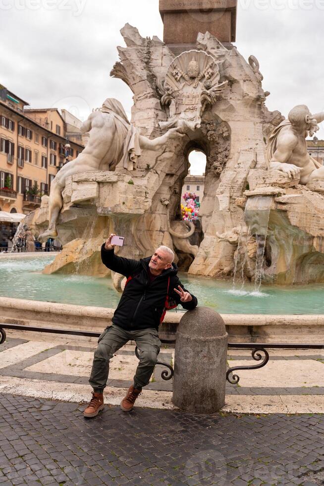 happy middle aged man on vacation taking a selfie in front of the fountain in piazza navona in rome photo