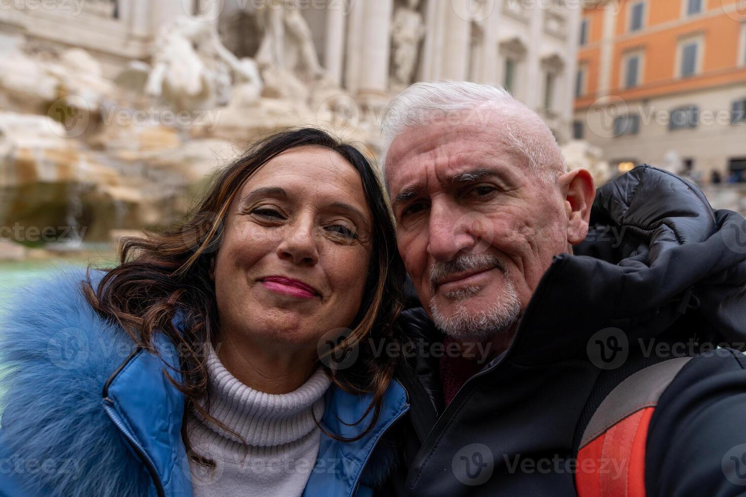 happy middle aged couple on vacation taking a selfie in front of a famous trevi fountain in rome photo