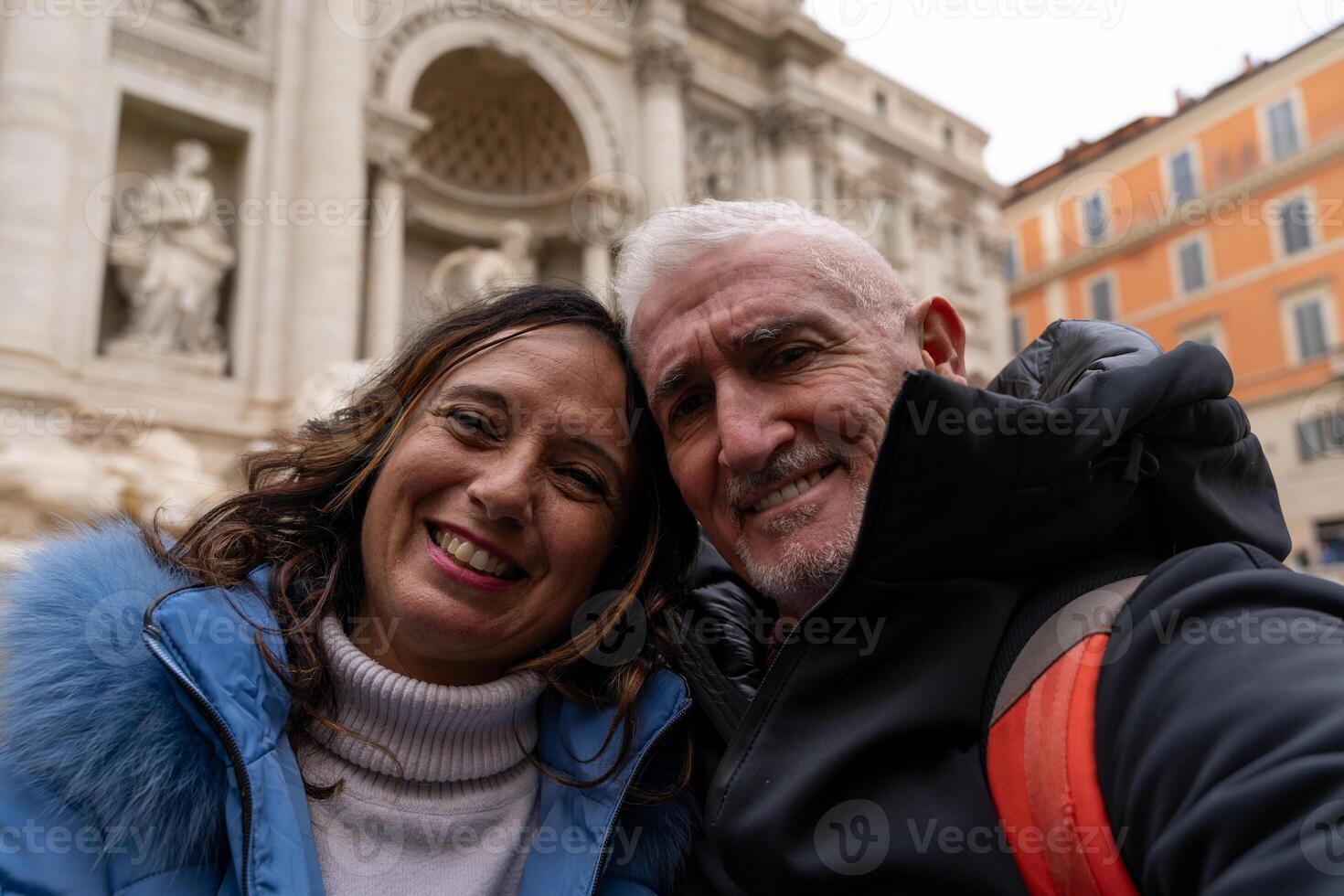 contento medio Envejecido Pareja en vacaciones tomando un selfie en frente de un famoso trevi fuente en Roma foto