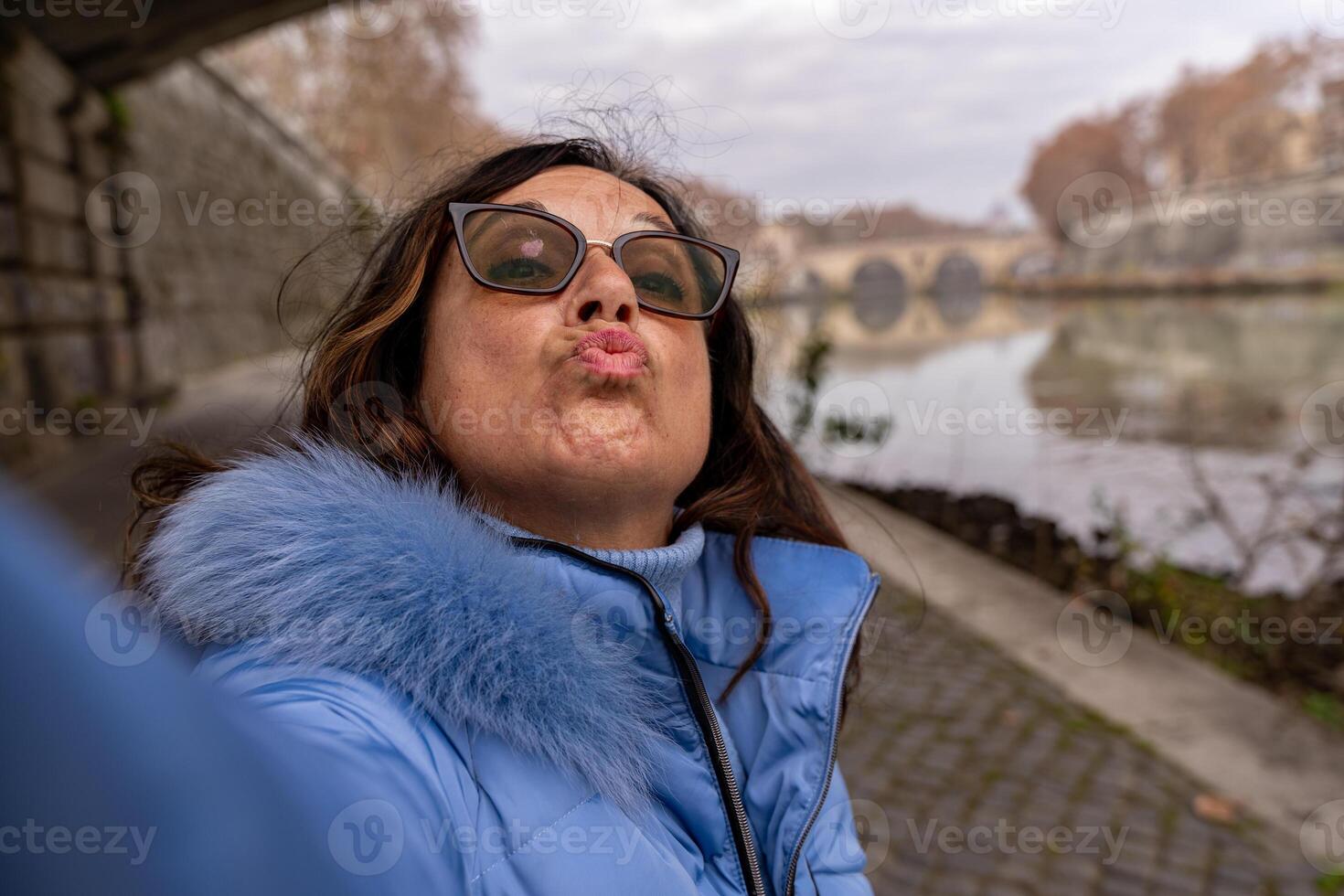 contento medio Envejecido mujer en vacaciones tomando un selfie en el bancos de el tiber río en Roma foto