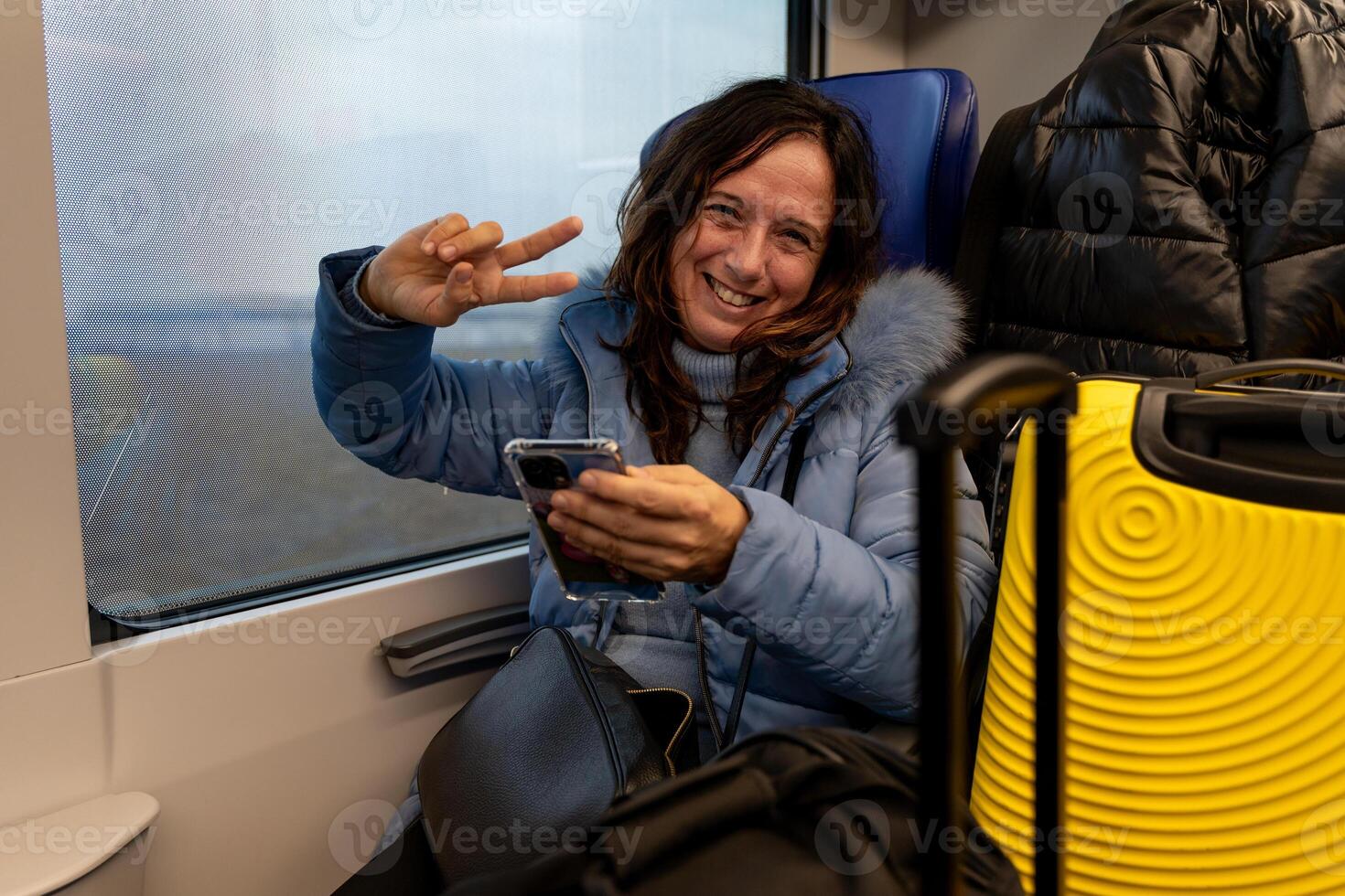 pretty middle-aged woman traveling on the train sitting among the luggage next to the window using the smart phone photo