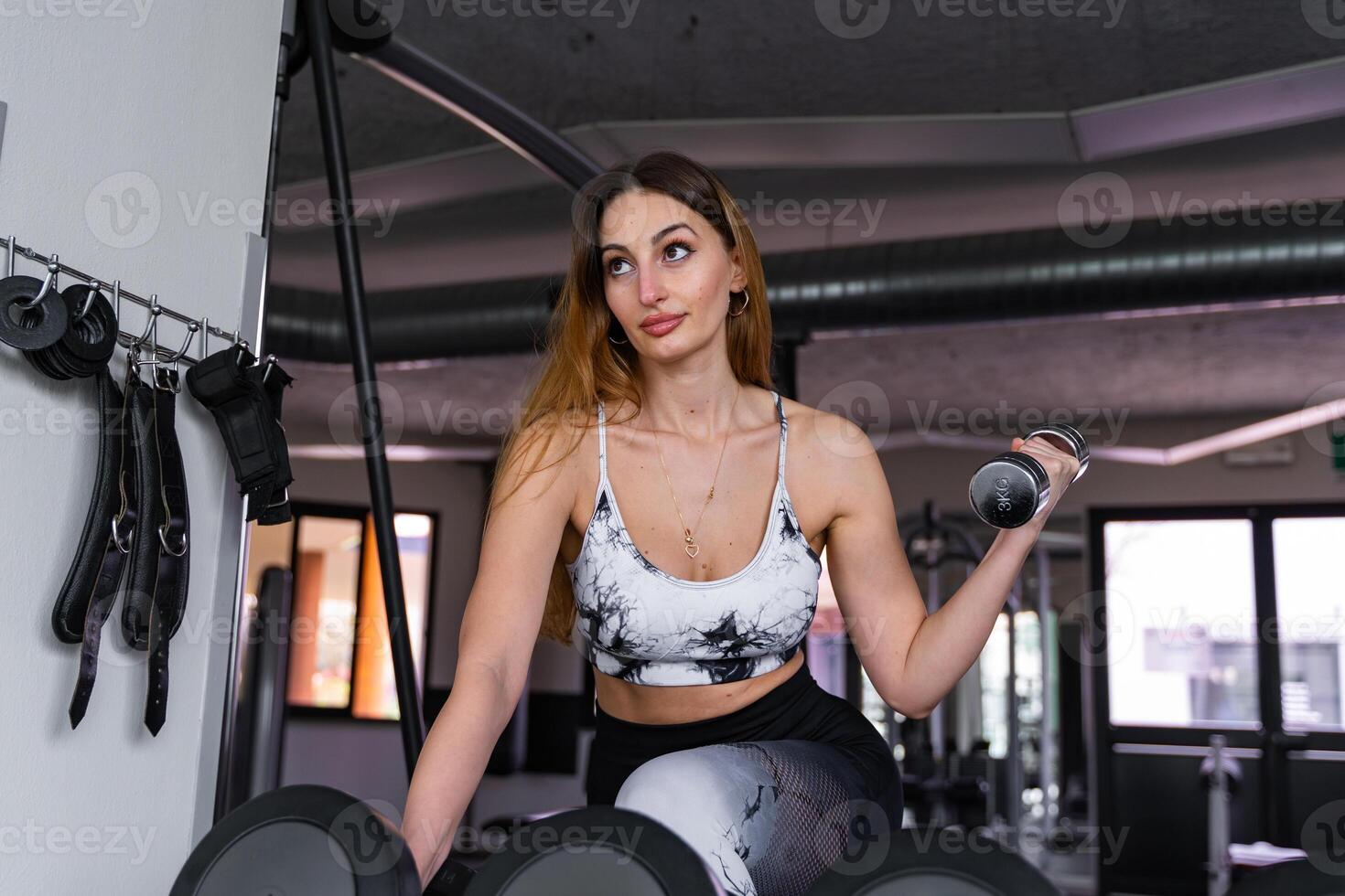 young charming blonde woman in sportswear lifting dumbbells in a gym photo