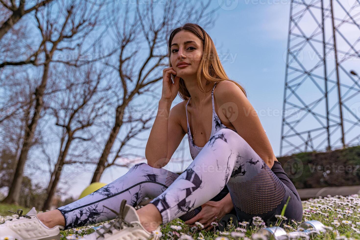 young beautiful blonde woman in tight sportswear doing light gymnastic exercises outdoors in a field of daisies photo