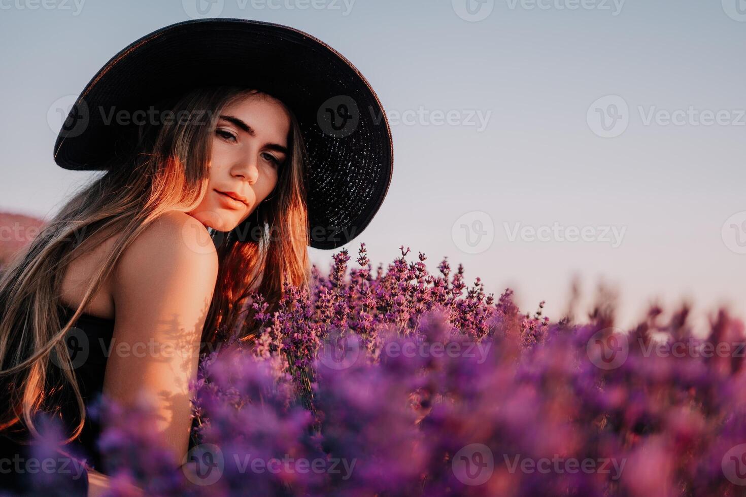 Woman lavender field. Happy carefree woman in black dress and hat with large brim smelling a blooming lavender on sunset. Perfect for inspirational and warm concepts in travel and wanderlust. Close up photo