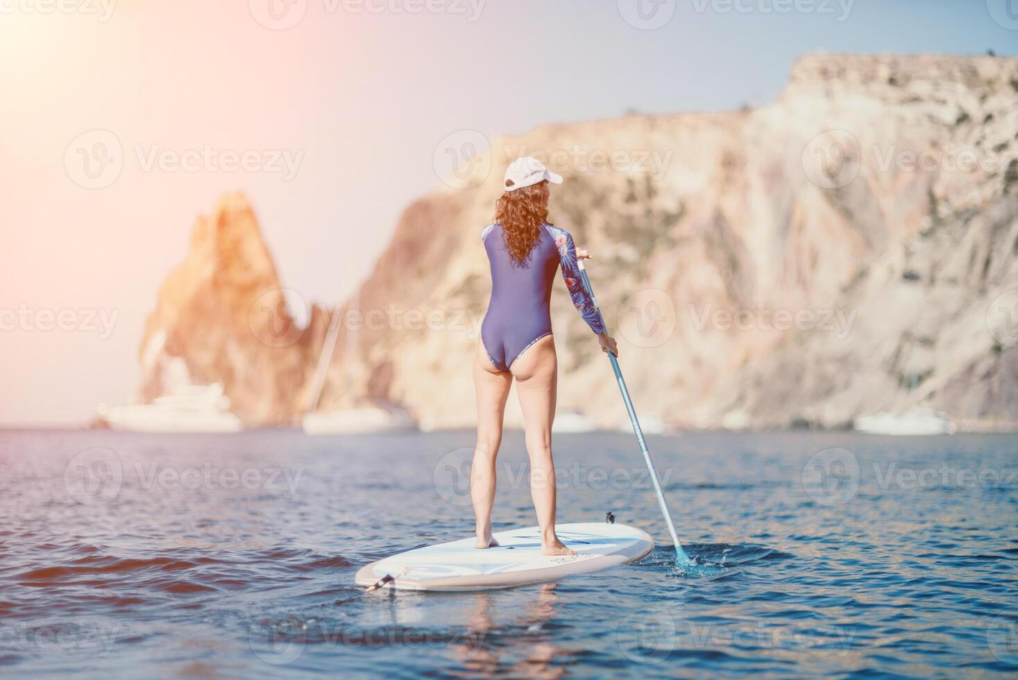 Woman sup yoga. Middle age sporty woman practising yoga pilates on paddle sup surfboard. Female stretching doing workout on sea water. Modern individual female hipster outdoor summer sport activity. photo