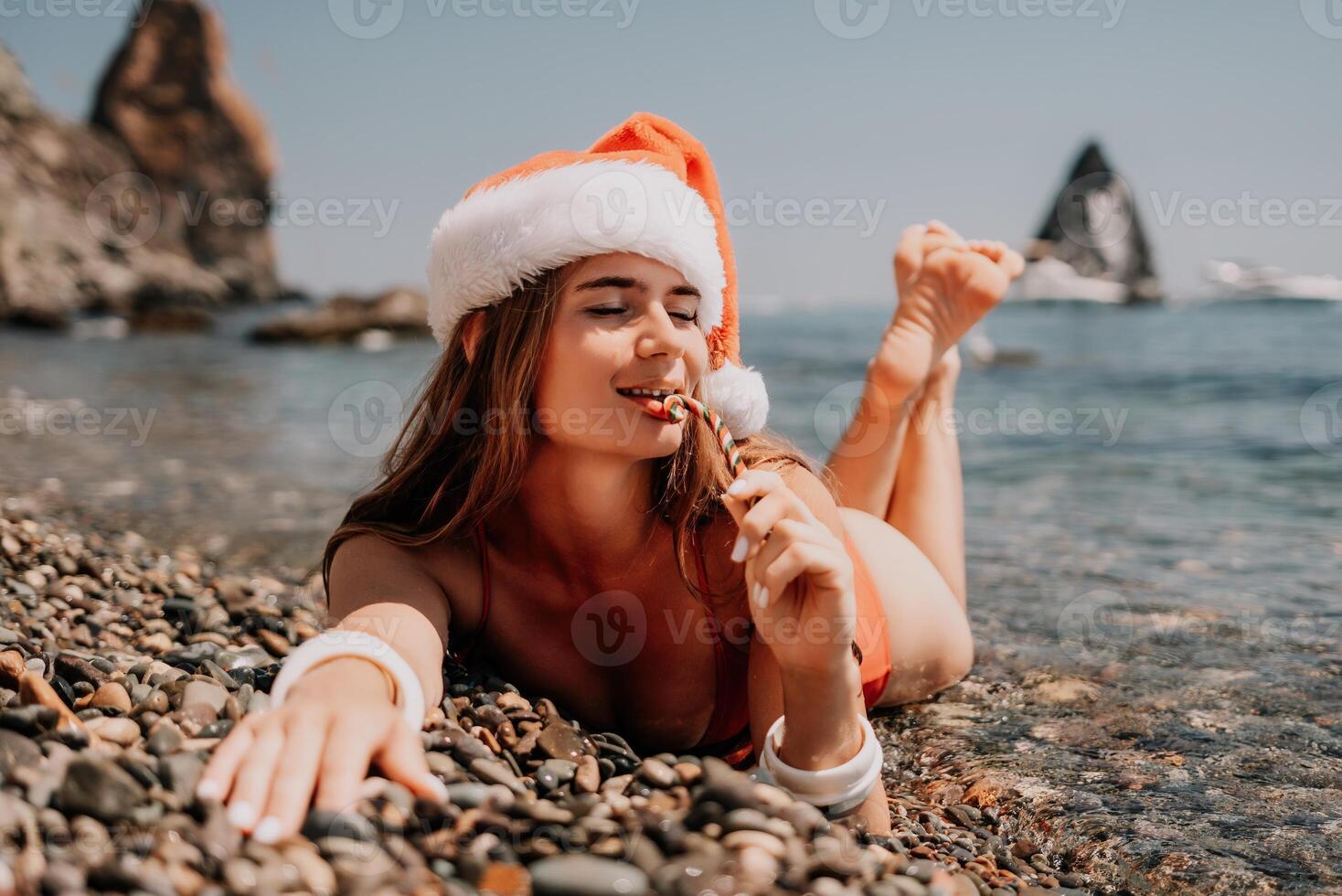 Woman travel sea. Happy tourist enjoy taking picture on the beach for memories. Woman traveler in Santa hat looks at camera on the sea bay, sharing travel adventure journey photo