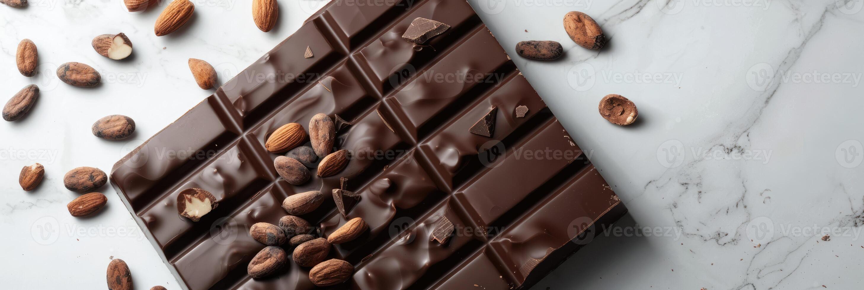 Chocolate bar with cacao beans and almonds scattered around it photo