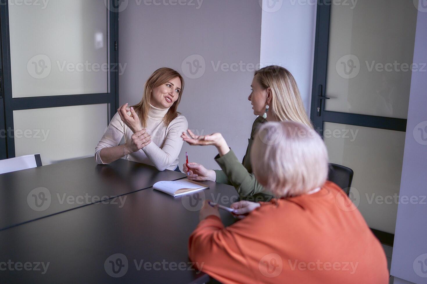 Tres mujer, incluso un persona con un discapacidad, discutir el de la empresa estrategia a un reunión en el oficina foto