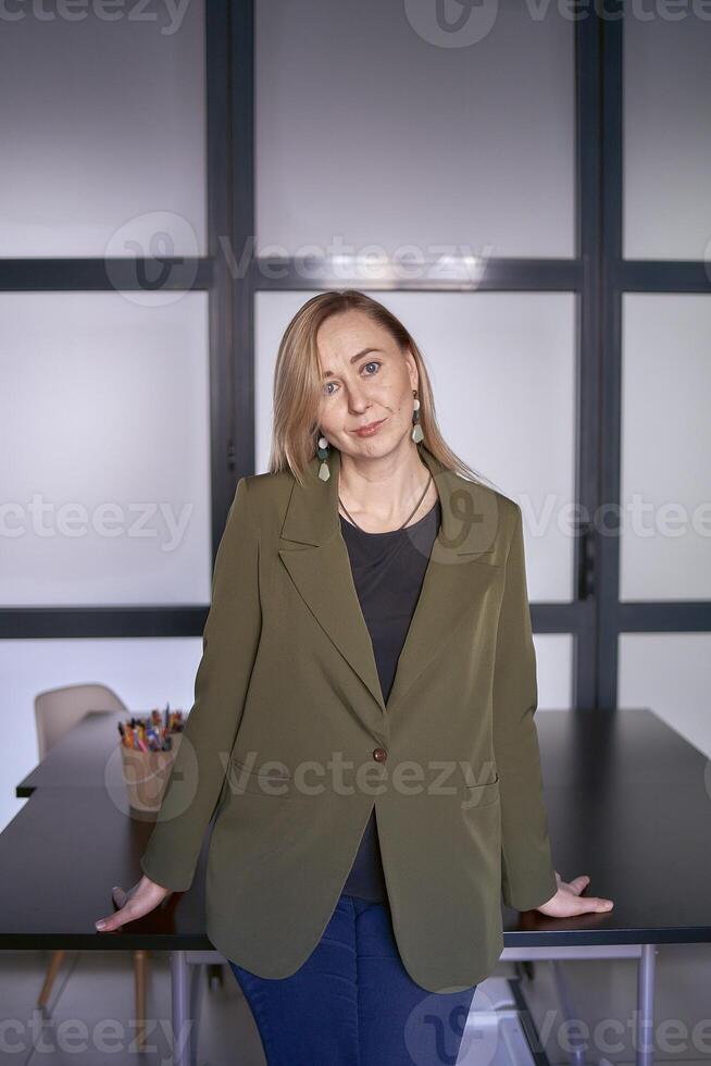 blonde woman with long hair in a green jacket and jeans in the office photo