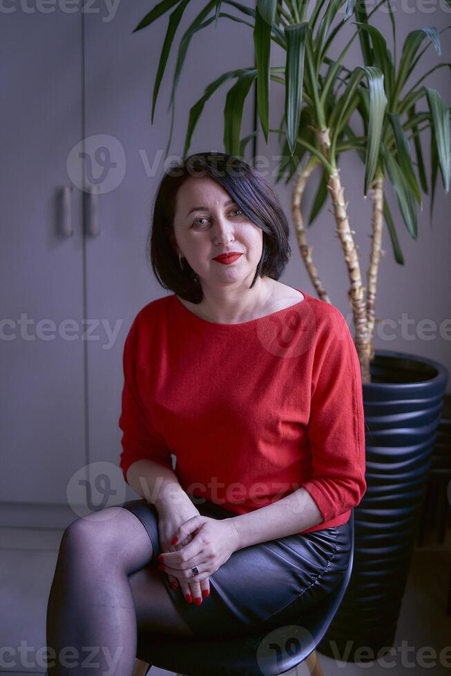 portrait of a brunette with a bob haircut in a red sweater and a leather mini skirt in the office photo