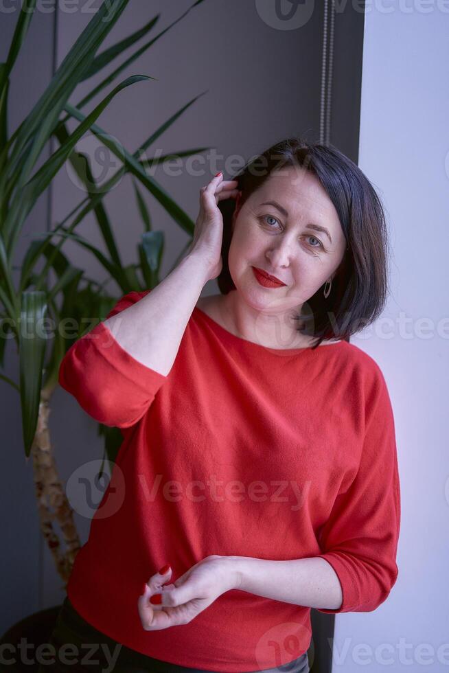 portrait of a brunette with a bob haircut in a red sweater and a leather mini skirt in the office photo
