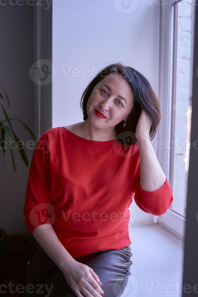 portrait of a brunette with a bob haircut in a red sweater and a leather mini skirt in the office photo