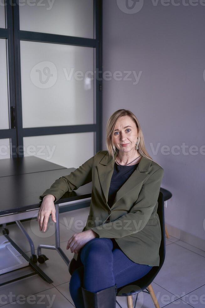 rubia mujer con largo pelo en un verde chaqueta y pantalones en el oficina foto