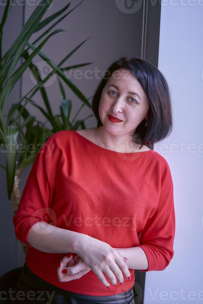 portrait of a brunette with a bob haircut in a red sweater and a leather mini skirt in the office photo